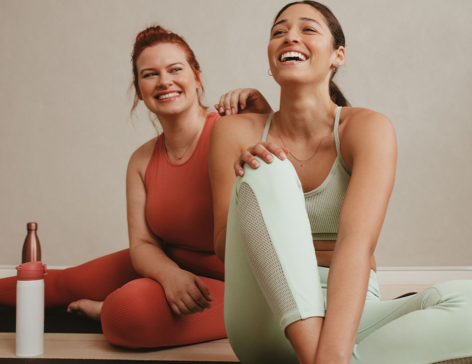 Two women sharing a laugh as they rest after a yoga session.