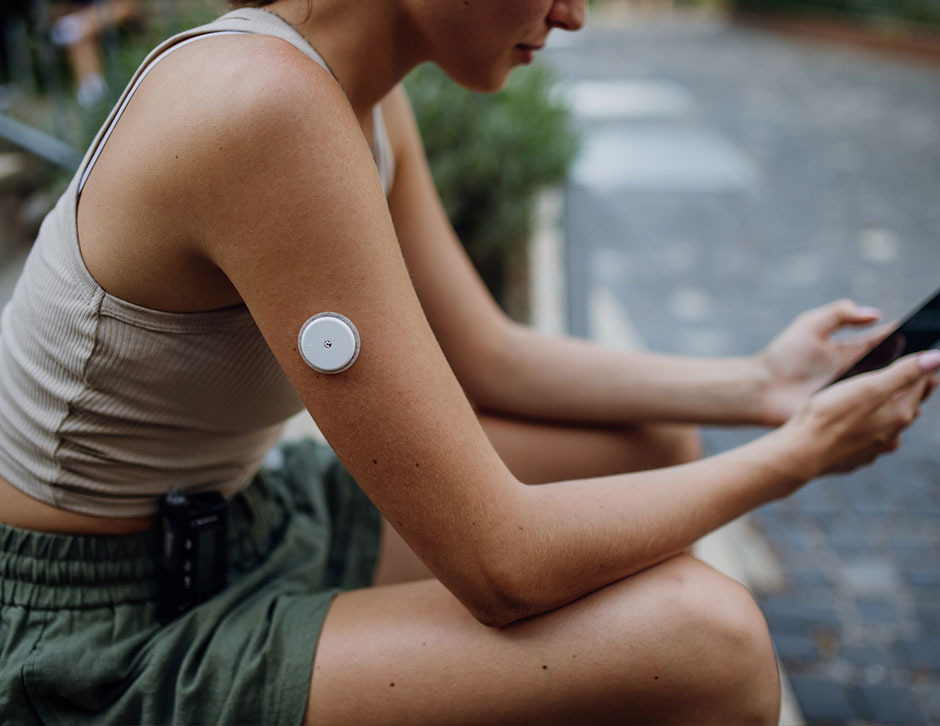 A side shot of a woman resting and checking her phone during a run, with the camera lens focused on the CGM device attached to her arm.