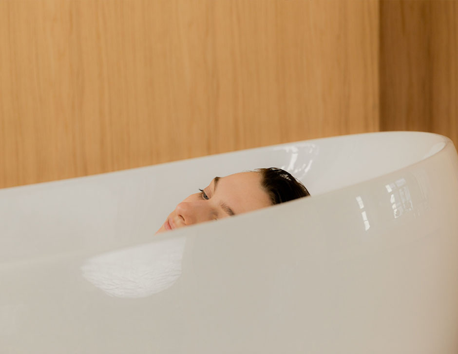 A woman taking a bath, peering lazily over the rim.