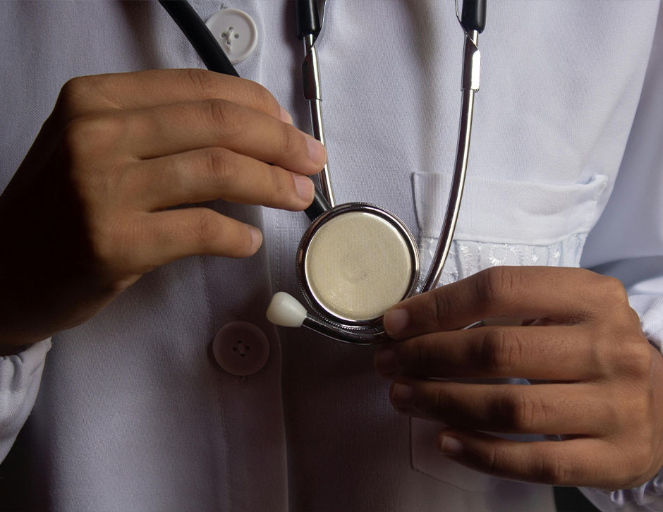 A close up of a doctor's chest as they hold a stethoscope while wearing a lab coat.